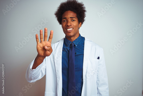 Young african american doctor man wearing coat standing over isolated white background showing and pointing up with fingers number four while smiling confident and happy.