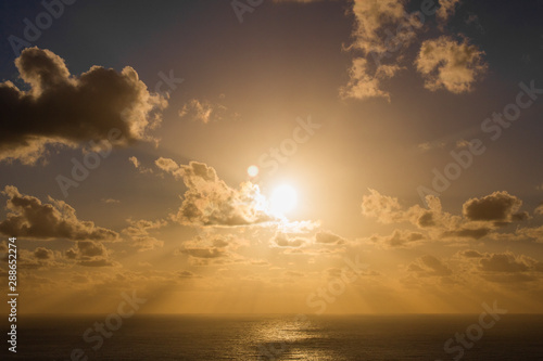 Dramatic golden rays over blue sunset or sunrise with clouds over the ocean.