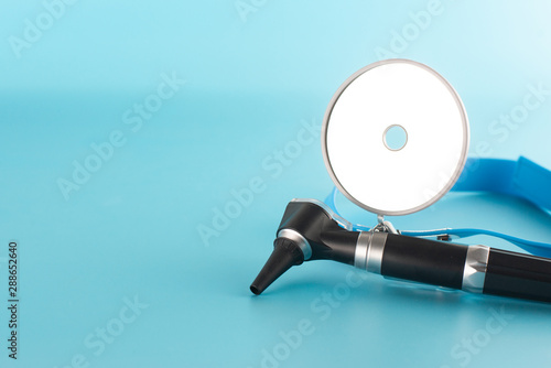 Otoscope with reflector mirror on blue background in health care concept.