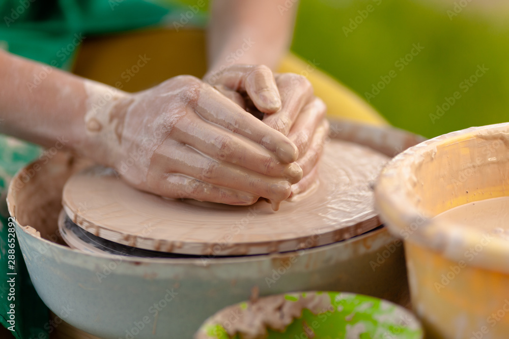 Hand craft making pottery on wheel. Female hands mold ceramic plate from clay (pot).