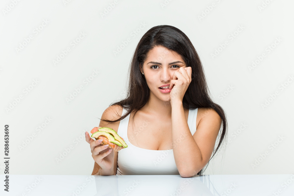 Young hispanic woman holding an avocado toast biting fingernails, nervous and very anxious. Young hispanic woman holding an avocado toast biting fingernails, nervous and very anxious.