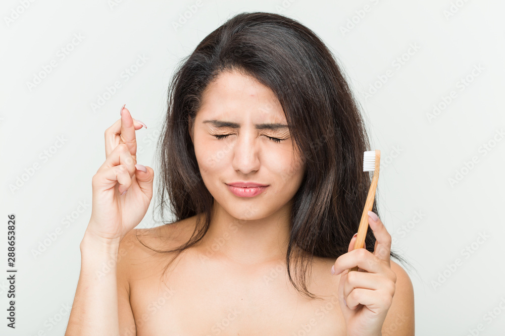 Young hispanic woman holding a toothbrush crossing fingers for having luck Young hispanic woman holding a toothbrush crossing fingers for having luck
