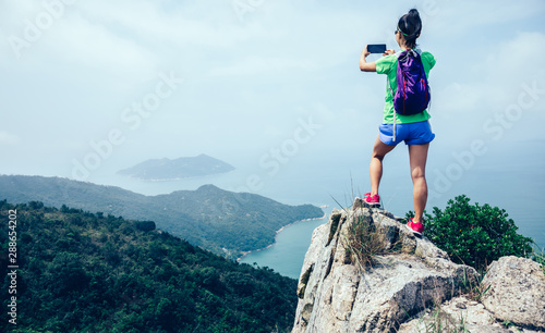 Successful Woman Hiker taking picture with smartphone In Seaside Mountain Top