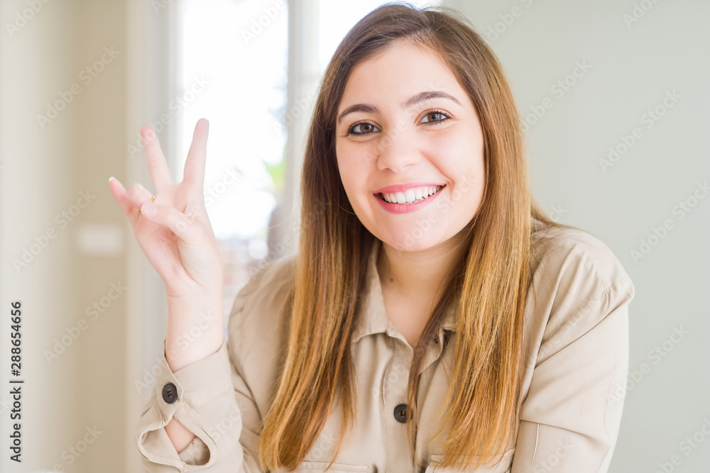 Beautiful young woman at home smiling with happy face winking at the camera doing victory sign. Number two. Beautiful young woman at home smiling with happy face winking at the camera doing victory sign. Number two.