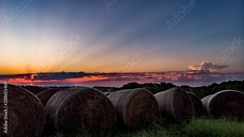 Sunrise in Nebraska over rows of round hay bales in a rural field