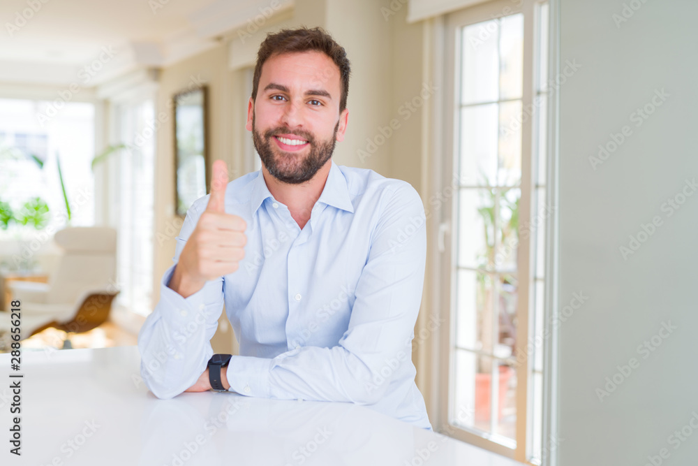 Handsome business man doing happy thumbs up gesture with hand. Approving expression looking at the camera with showing success.