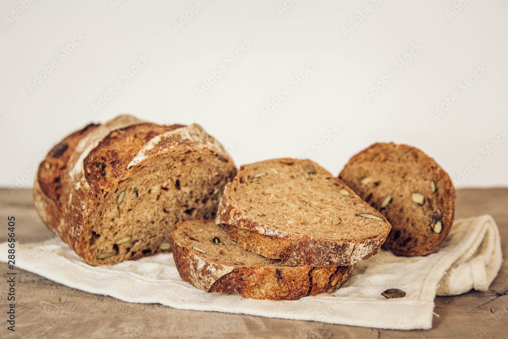 Brown fresh bread with seeds are cut into pieces on old wood background. Top view, copy space