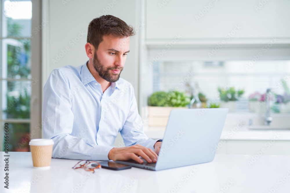 Handsome man working using computer laptop and drinking a cup of coffee with a confident expression on smart face thinking serious Handsome man working using computer laptop and drinking a cup of coffee with a confident expression on smart face thinking serious