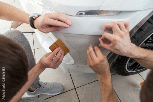 Retrofitting the car with a solid transparent protective film, the master smooths the surface by squeezing air bubbles with a scraper, protecting the vehicles from scratches and chips in the workshop