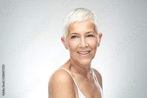 Beautiful smiling senior woman with short gray hair posing in front of gray background. Beauty photography.