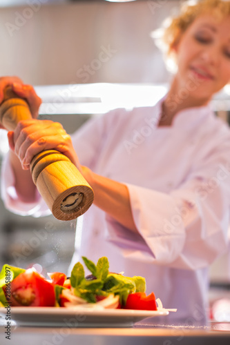 Mature chef using peppermill on salad in plate at restaurant