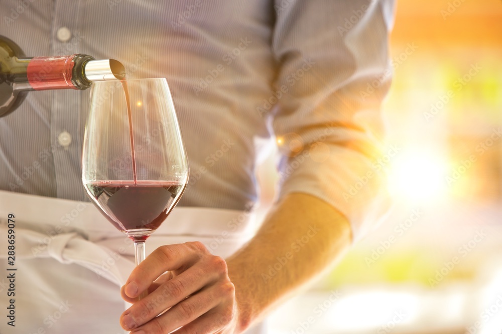 Midsection of waiter pouring red wine in wineglass at restaurant Midsection of waiter pouring red wine in wineglass at restaurant
