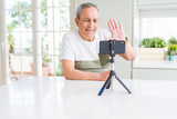 Handsome senior man waving hello to the smartphone camera doing video smiling very happy