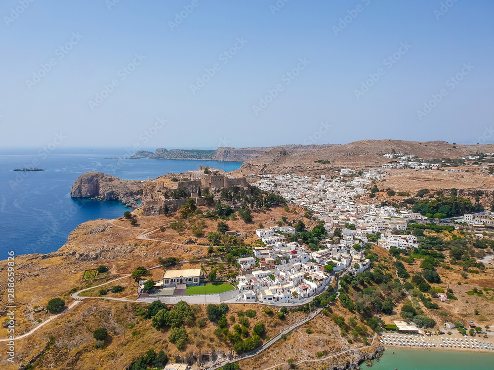 Aerial birds eye view drone photo of village Lindos, Rhodes island, Dodecanese, Greece. Sunset panorama with castle, Mediterranean sea coast. Famous tourist destination in South Europe.