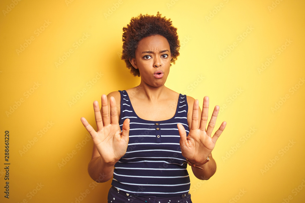 Beauitul african american woman wearing summer t-shirt over isolated yellow background Moving away hands palms showing refusal and denial with afraid and disgusting expression. Stop and forbidden. Beauitul african american woman wearing summer t-shirt over isolated yellow background Moving away hands palms showing refusal and denial with afraid and disgusting expression. Stop and forbidden.