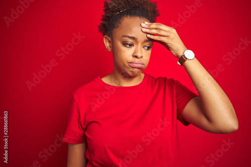 Young beautiful african american woman with afro hair over isolated red background worried and stressed about a problem with hand on forehead, nervous and anxious for crisis