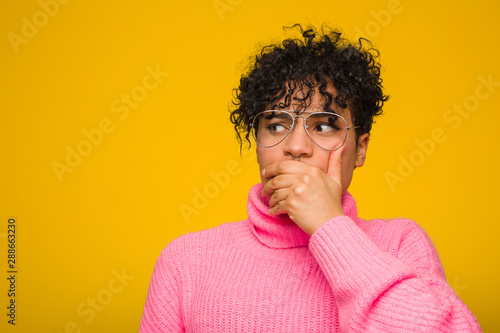 Young african american woman wearing a pink sweater thoughtful looking to a copy space covering mouth with hand.