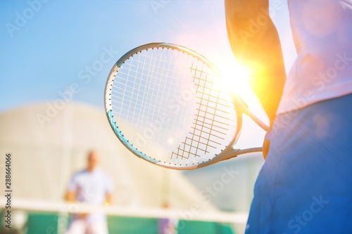 Photo of mature man holding tennis racket against friend playing match on court