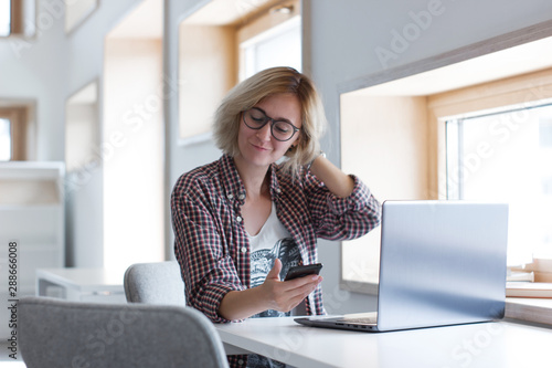 Girl with laptop using smartphone. Online learning distance course. Distance education concept. Portrait of working freelancer girl in modern co-working space. Student learning in library. Blogger.