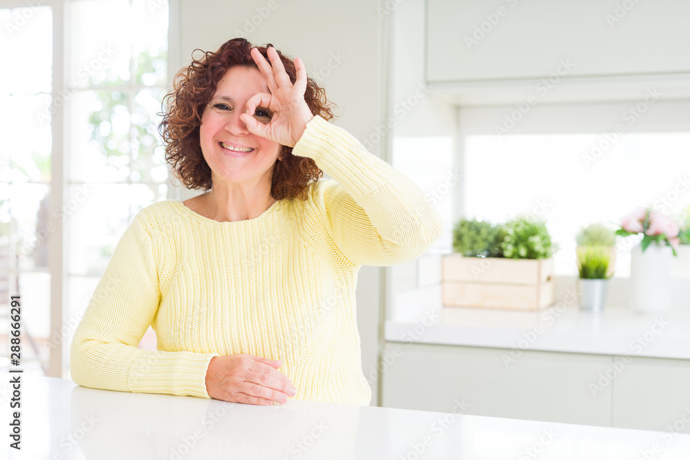Beautiful senior woman wearing yellow sweater doing ok gesture with hand smiling, eye looking through fingers with happy face. Beautiful senior woman wearing yellow sweater doing ok gesture with hand smiling, eye looking through fingers with happy face.
