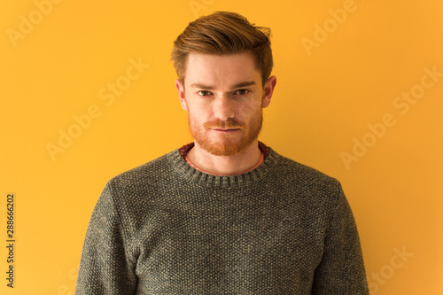 Young redhead man against an orange wall