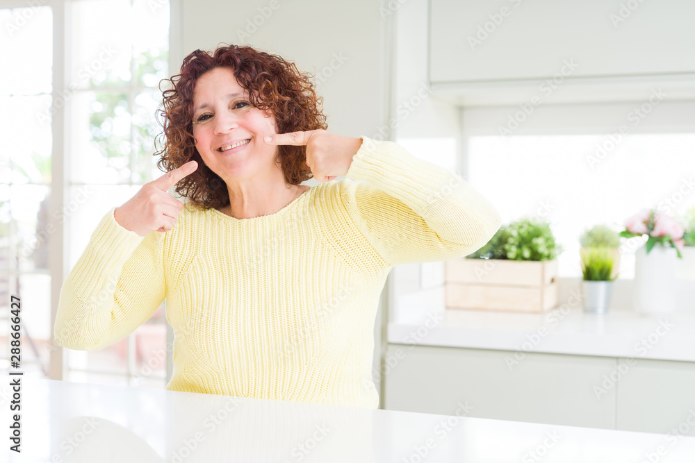 Beautiful senior woman wearing yellow sweater smiling confident showing and pointing with fingers teeth and mouth. Health concept. Beautiful senior woman wearing yellow sweater smiling confident showing and pointing with fingers teeth and mouth. Health concept.