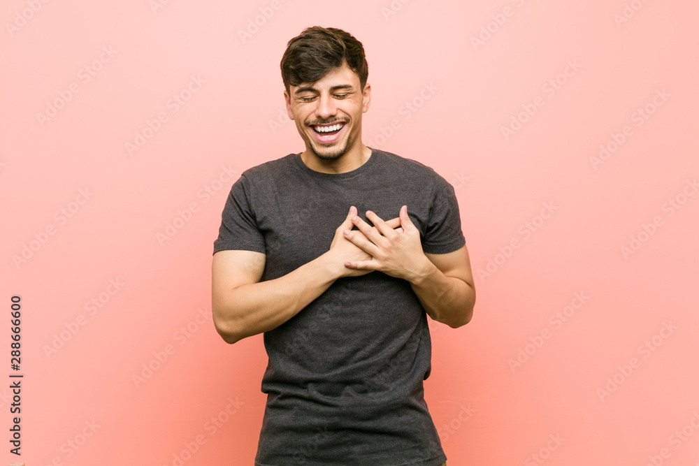Young hispanic casual man laughing keeping hands on heart, concept of happiness. - obrazy, fototapety, plakaty 
