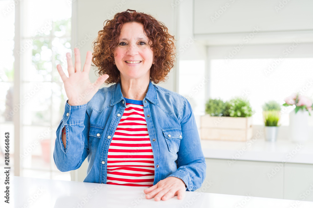 Middle age senior woman with curly hair wearing denim jacket at home showing and pointing up with fingers number five while smiling confident and happy. Middle age senior woman with curly hair wearing denim jacket at home showing and pointing up with fingers number five while smiling confident and happy.