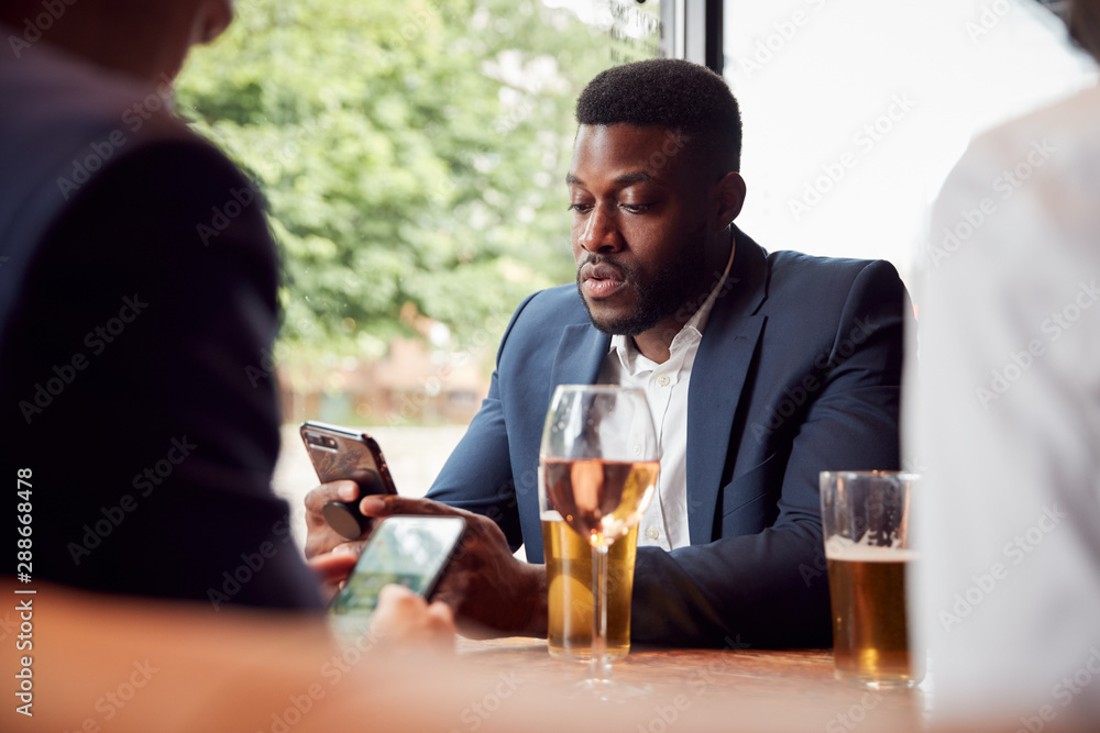 Group Of Business Colleagues All Checking Mobile Phones Whilst Meeting For Drink In Bar Group Of Business Colleagues All Checking Mobile Phones Whilst Meeting For Drink In Bar