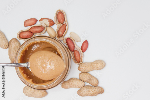 Creamy peanut butter in glass jar  peanut and spoon isolated on white background. A traditional product of American cuisine