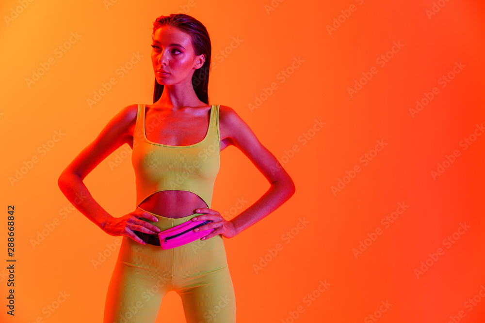 Naklejka premium Photo of fitness brunette woman wearing formfitting sportswear standing with arms on waist