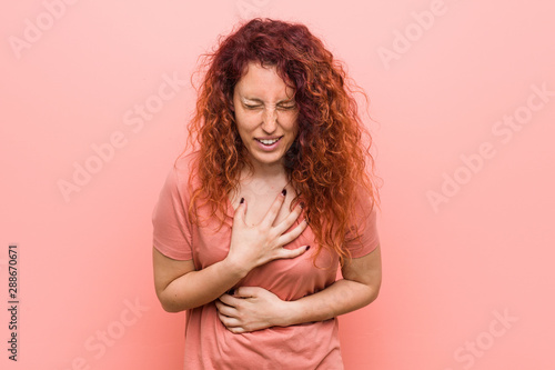 Young natural and authentic redhead woman laughs happily and has fun keeping hands on stomach.