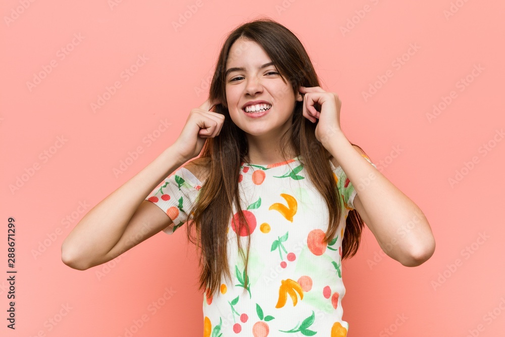 Girl wearing a summer clothes against a red wall covering ears with hands. Girl wearing a summer clothes against a red wall covering ears with hands.