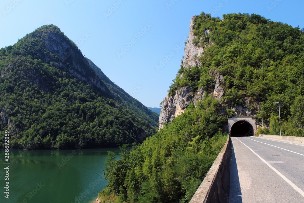 Road and tunnel over the Drina river canyon (Bosnia and Herzegovina) surrounded by mountains covered by trees in summer