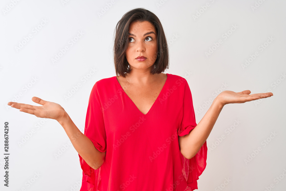 Young beautiful woman wearing red t-shirt standing over isolated white background clueless and confused expression with arms and hands raised. Doubt concept.