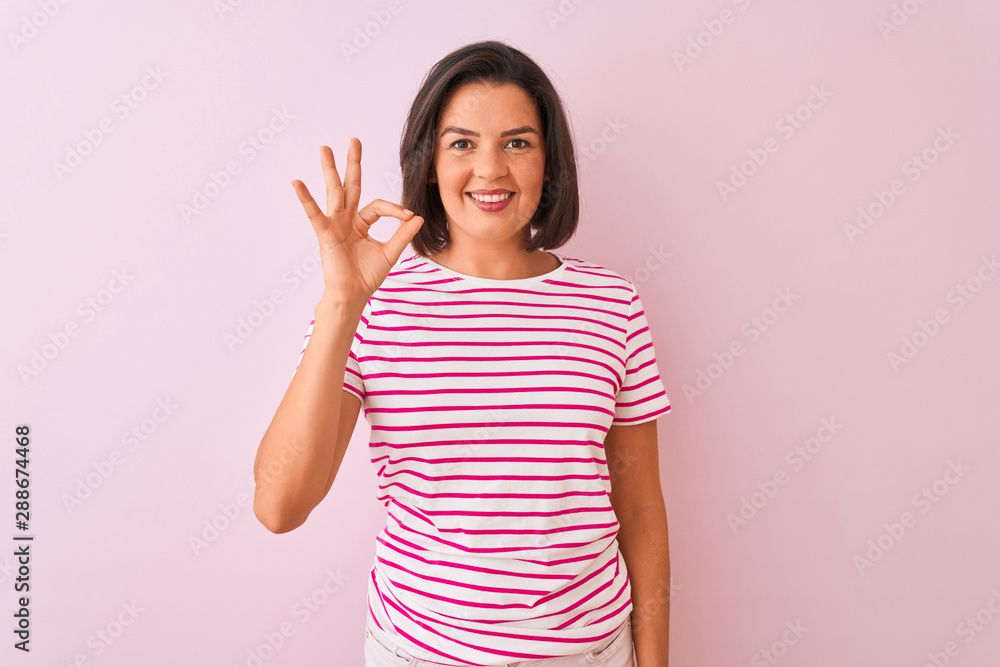 Young beautiful woman wearing striped t-shirt standing over isolated pink background smiling positive doing ok sign with hand and fingers. Successful expression. Young beautiful woman wearing striped t-shirt standing over isolated pink background smiling positive doing ok sign with hand and fingers. Successful expression.