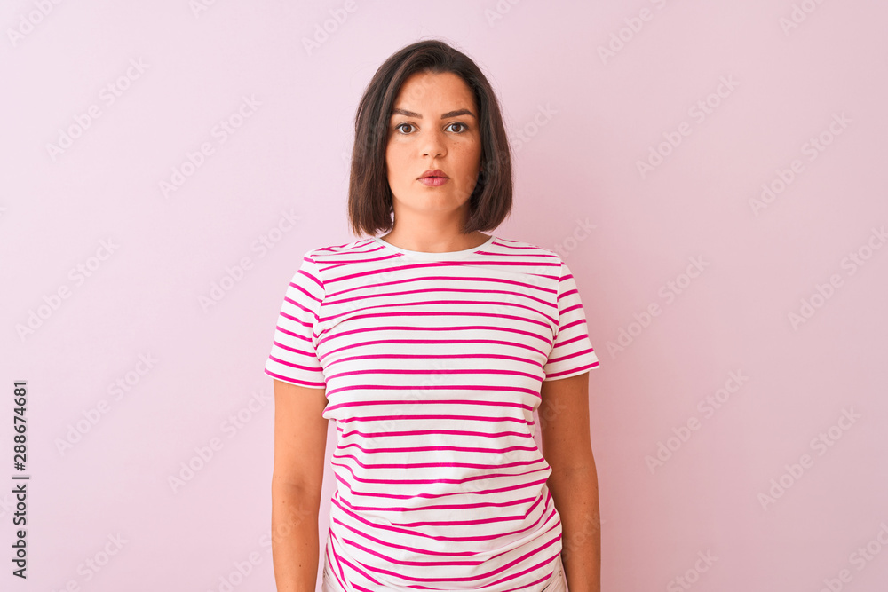 Fototapeta premium Young beautiful woman wearing striped t-shirt standing over isolated pink background Relaxed with serious expression on face. Simple and natural looking at the camera.