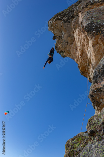 girl hanging on the edge of a cliff upside down with outstretched arm. Climber fall from a cliff on a safety rope. extreme climbing. extreme sport, winter season. rocks and blue sky on the background