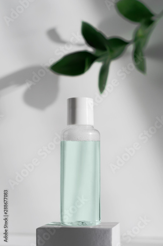Makeup remover, natural moisturizing lotion mockup close up. Transparent liquid container side view. Organic cosmetics poster concept. Micellar water bottle and blurred leaves on background