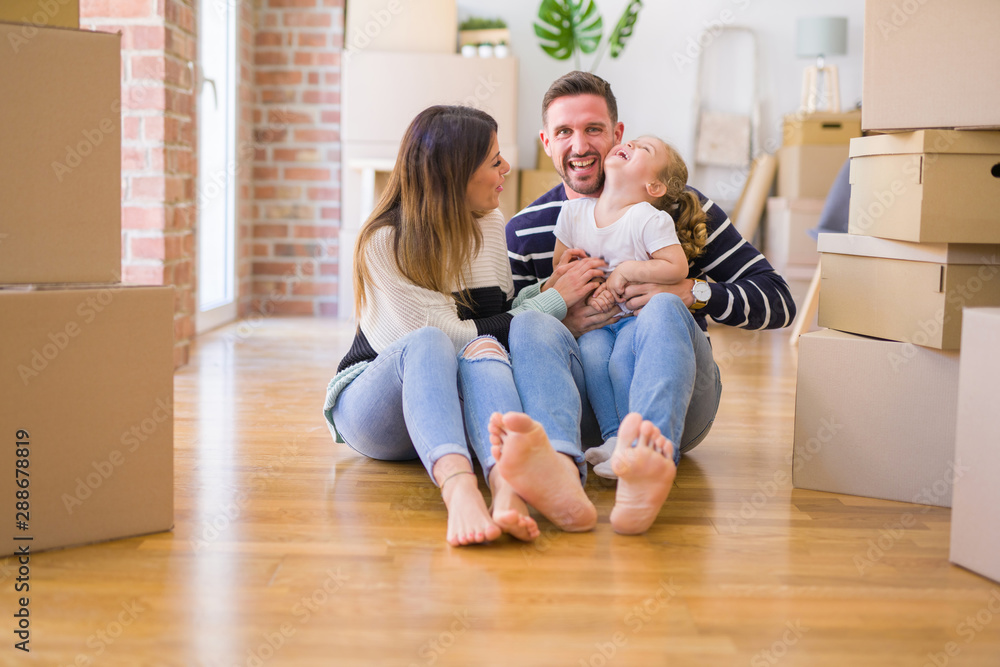 Beautiful family sitting on the floor playing with his kid at new home around cardboard boxes Beautiful family sitting on the floor playing with his kid at new home around cardboard boxes