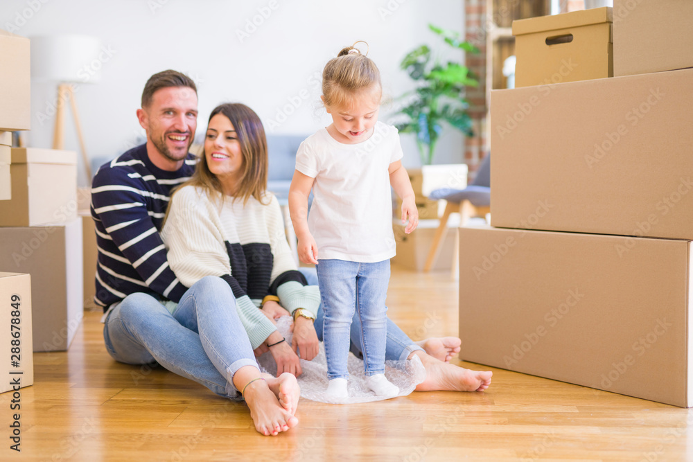 Beautiful family sitting on the floor playing with his kid at new home around cardboard boxes Beautiful family sitting on the floor playing with his kid at new home around cardboard boxes
