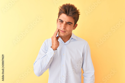 Young handsome businessman wearing elegant shirt over isolated yellow background touching mouth with hand with painful expression because of toothache or dental illness on teeth. Dentist concept.