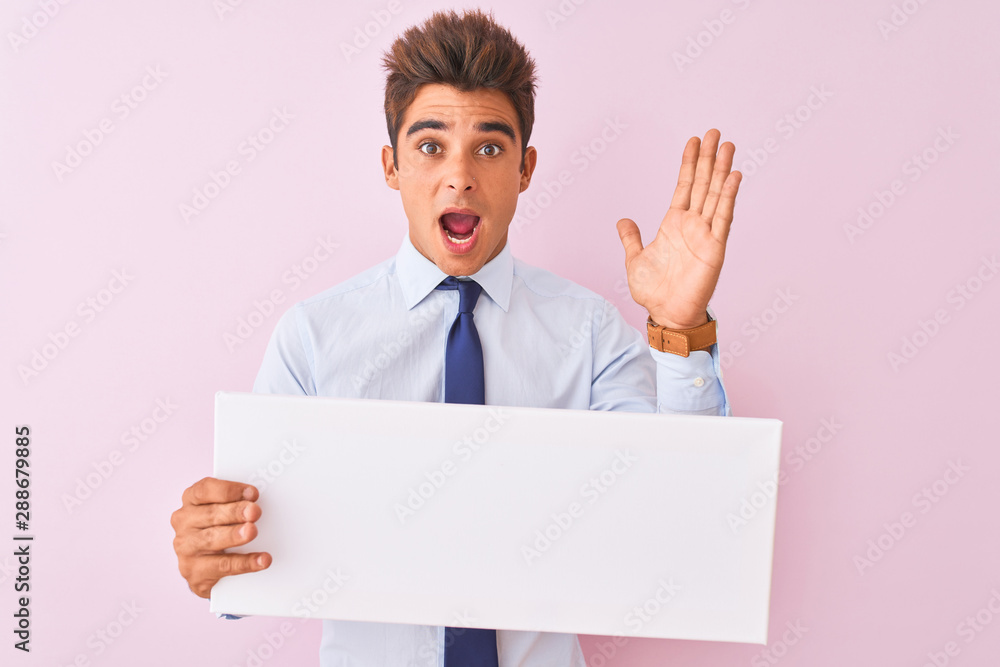 Young handsome businessman holding banner standing over isolated pink background very happy and excited, winner expression celebrating victory screaming with big smile and raised hands Young handsome businessman holding banner standing over isolated pink background very happy and excited, winner expression celebrating victory screaming with big smile and raised hands
