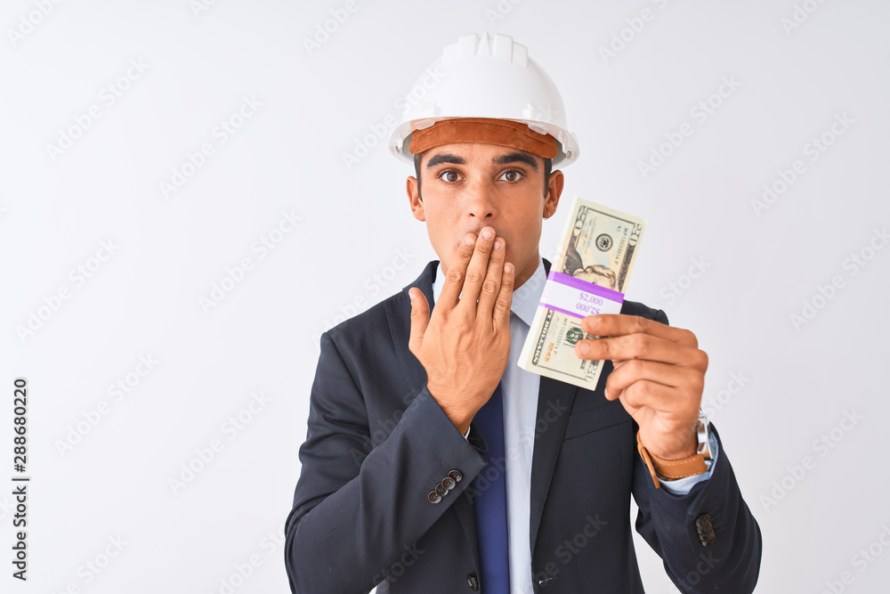 Young handsome architect man wearing helmet holding dollars over isolated white background cover mouth with hand shocked with shame for mistake, expression of fear, scared in silence, secret concept Young handsome architect man wearing helmet holding dollars over isolated white background cover mouth with hand shocked with shame for mistake, expression of fear, scared in silence, secret concept