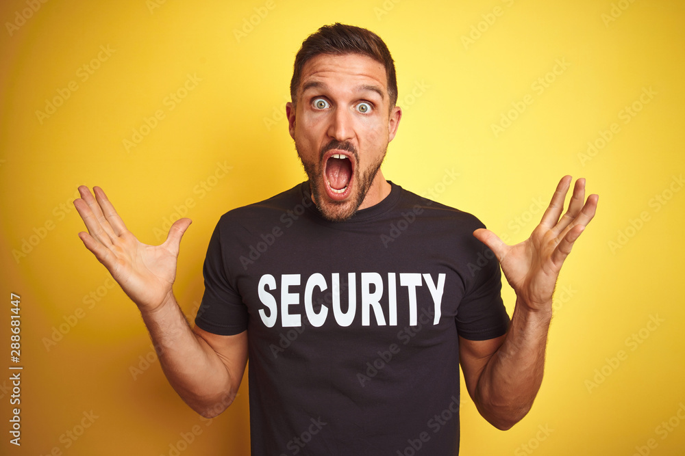 Young safeguard man wearing security uniform over yellow isolated background celebrating crazy and amazed for success with arms raised and open eyes screaming excited. Winner concept Young safeguard man wearing security uniform over yellow isolated background celebrating crazy and amazed for success with arms raised and open eyes screaming excited. Winner concept