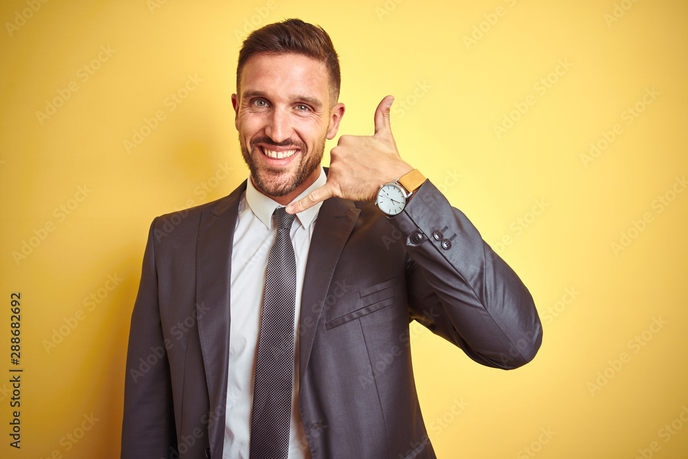 Young handsome business man over yellow isolated background smiling doing phone gesture with hand and fingers like talking on the telephone. Communicating concepts. Young handsome business man over yellow isolated background smiling doing phone gesture with hand and fingers like talking on the telephone. Communicating concepts.