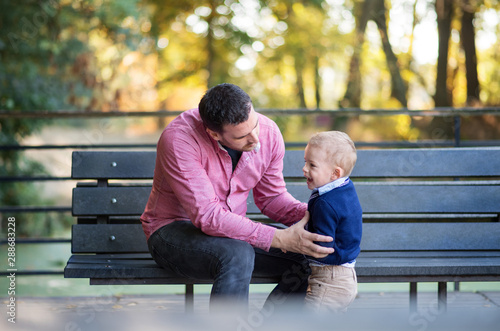Father with small son sitting on bench in park in autumn.