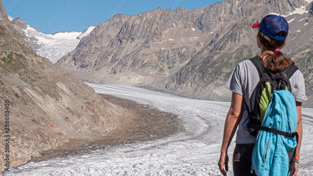 A lone female hiker treks next to the famous aletsch glacier in central Switzerland. The glacier carves a path through the high alpine mountain environment. A lone female hiker treks next to the famous aletsch glacier in central Switzerland. The glacier carves a path through the high alpine mountain environment.