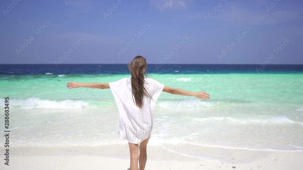 Beautiful brunette girl in a white dress walks on the white sand beach to Turquoise sea in the Maldives. Blue sky. Summer. Happiness. Freedom. Slow motion. Beautiful brunette girl in a white dress walks on the white sand beach to Turquoise sea in the Maldives. Blue sky. Summer. Happiness. Freedom. Slow motion.