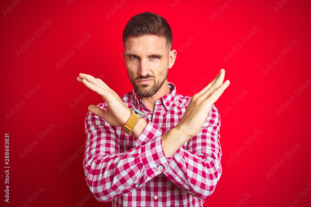 Fototapeta premium Young handsome man over red isolated background Rejection expression crossing arms doing negative sign, angry face